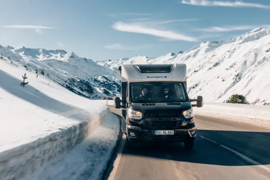 Camper die op de weg rijdt langs besneeuwde bergen